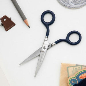 A small stainless steel scissors with navy blue handles, open on a desktop.